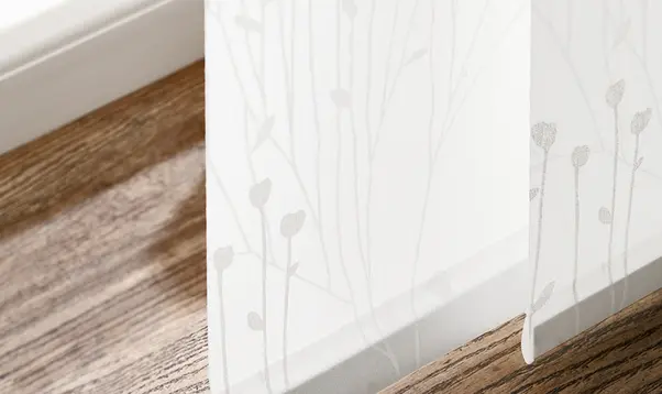 Nahaufnahme eines transparenten weissen Stoffes mit dezentem Blumenmuster vor Holzfussboden