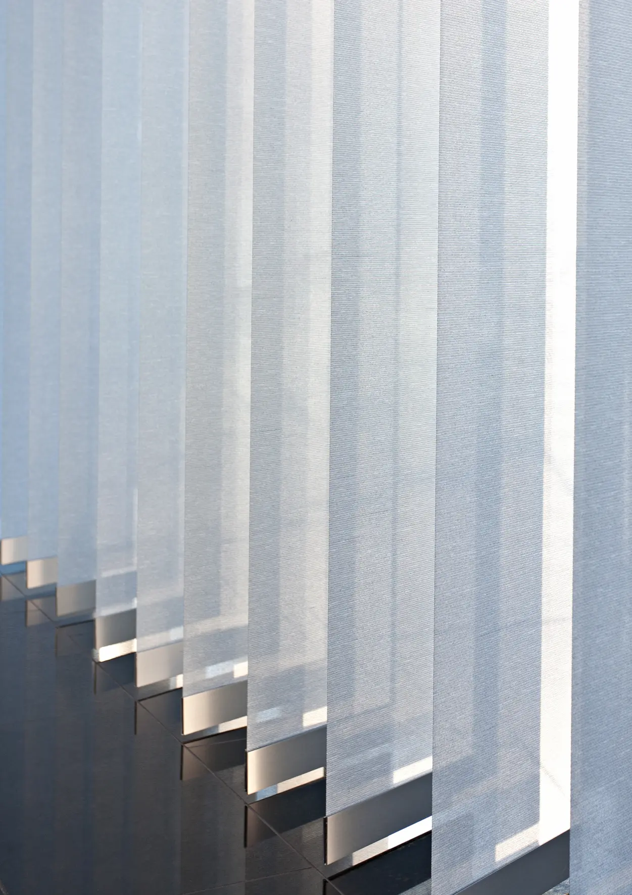 Nahaufnahme von halbtransparenten vertikalen Fenstervorhängen mit Licht- und Schattenspiel auf einem glänzenden Boden