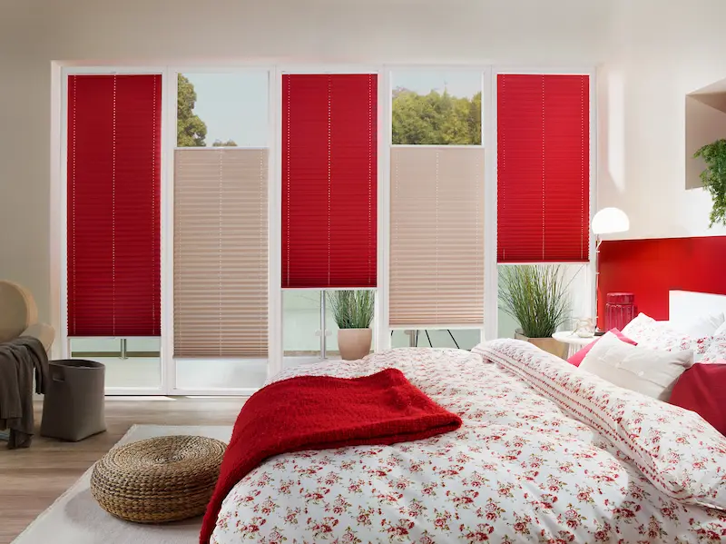 Grosse Fenster im Schlafzimmer mit roten und beigen Faltstoffen als Sicht und Lichtschutz