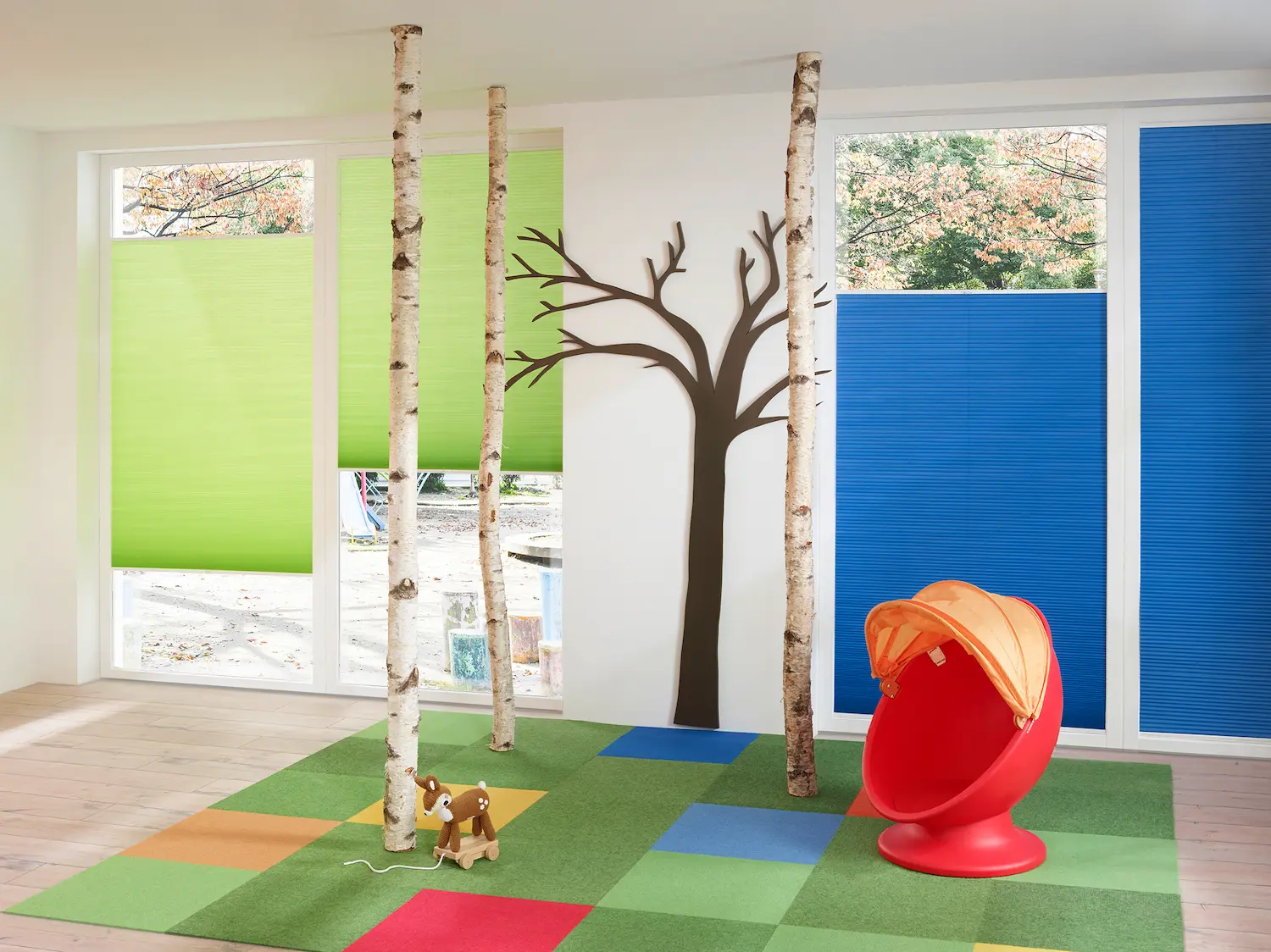 Spielzimmer mit grünen und blauen Faltstoffen an grossen Fenstern als farbenfroher Lichtschutz