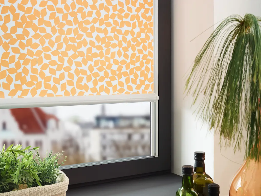 Nahaufnahme eines Fensters mit modernem Rollo im orangefarbenen Blättermuster als dekorativer Sichtschutz in der Küche