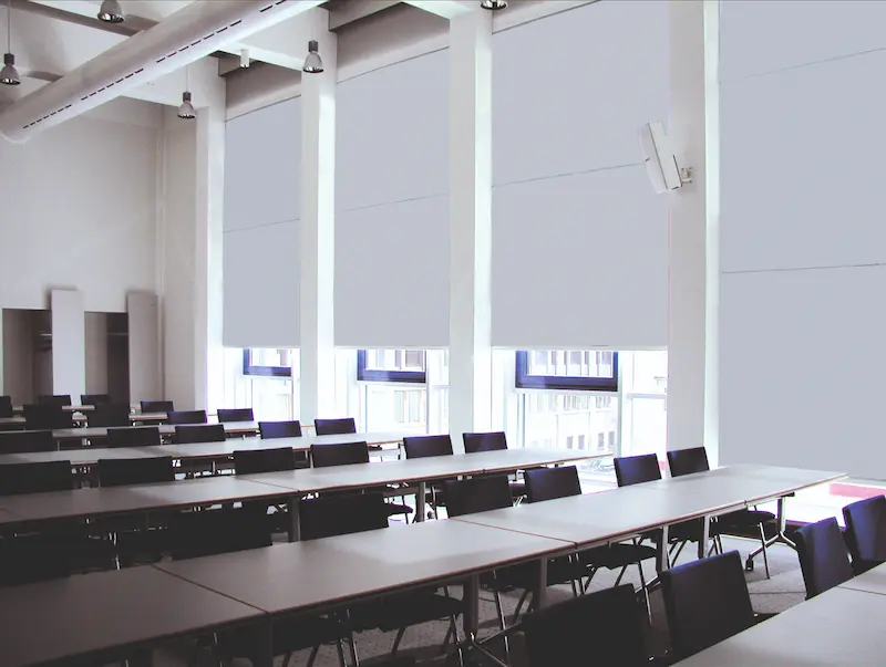 Grosser Raum mit mehreren Tischen und hellen Stoffanlagen vor hohen Fenstern